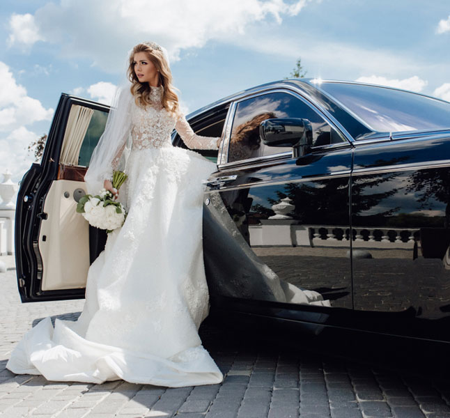 Bride wearing a white gown is exiting out of a luxurious limousine for special occasion